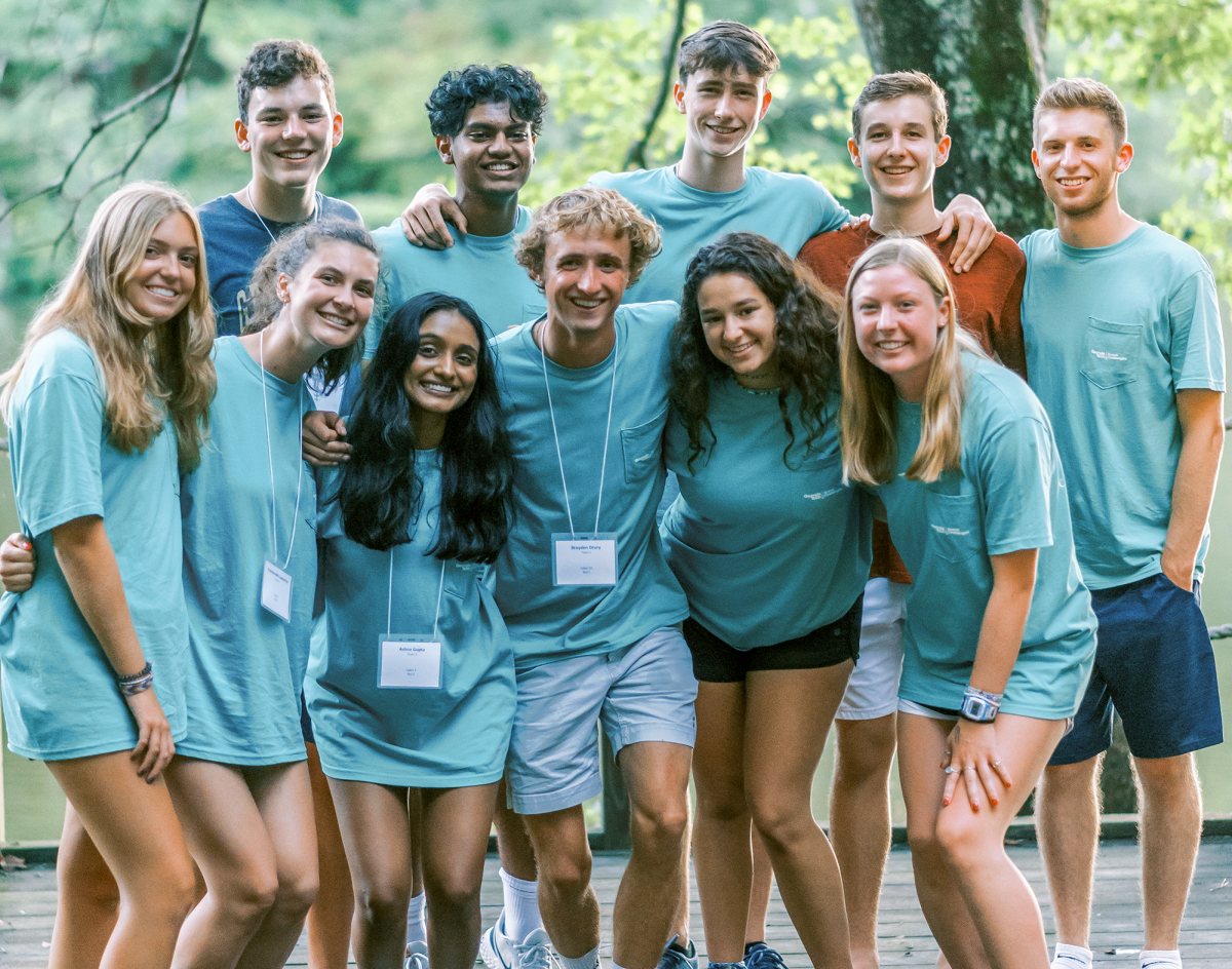 A group of students of different races smiling to the camera with a leafy backdrop.